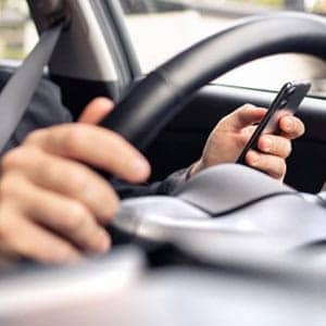 A man using his cell phone while driving a car - The Law Man Group, APC